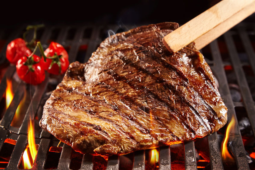 Wooden tongs picking up beef on grill